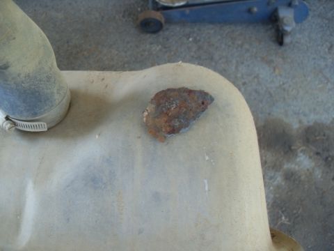 1990 Ford Bronco - A small, rusted fragment is stuck to the top of a vehicle's fuel tank, with a hose clamp nearby.