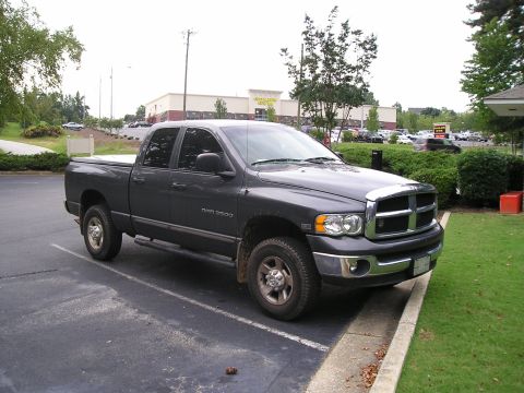 1989 Ford Bronco - A dark gray Dodge Ram 2500 pickup truck is parked in a lot with a building and trees in the background.