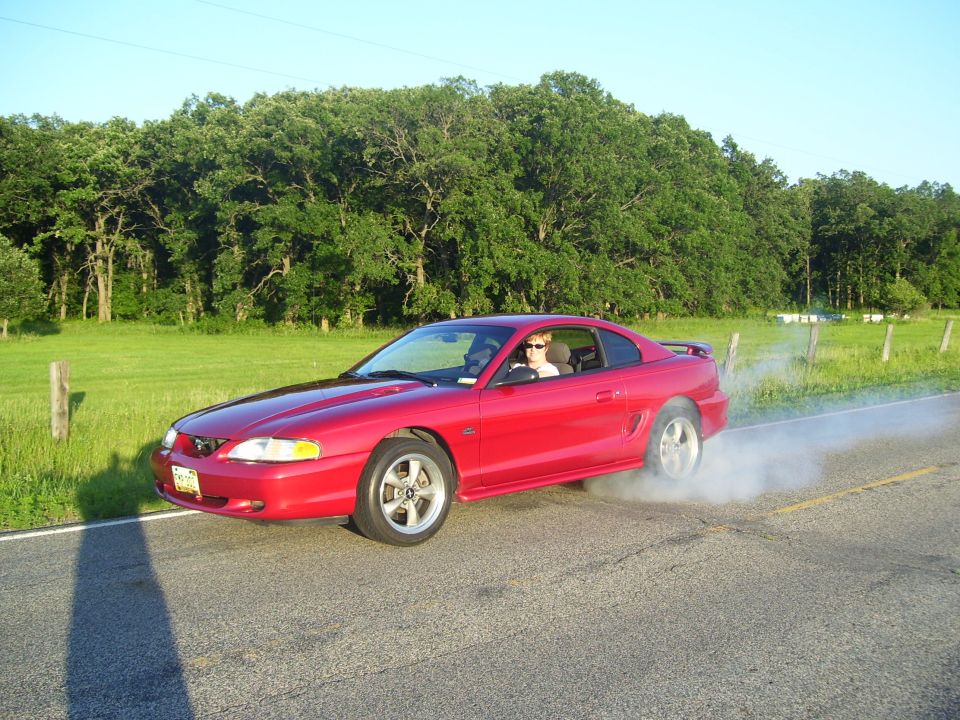Red Ford Mustang coupe doing a burnout with tire smoke on a rural road