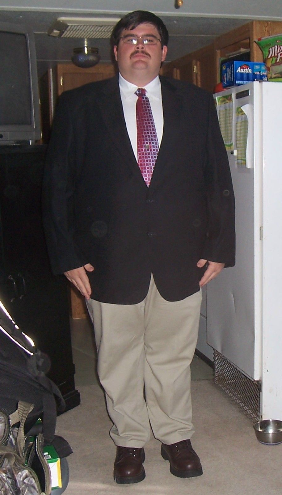 Man wearing a black suit jacket, white shirt, patterned tie, and tan pants, standing indoors