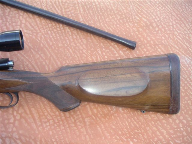 Wooden rifle stock with a scope and barrel on a textured surface