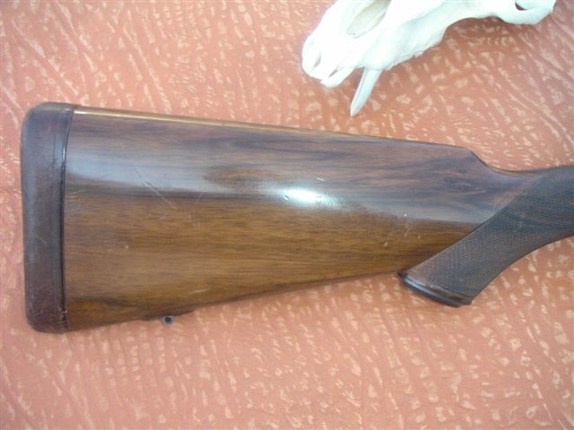 Wooden gun stock with dark butt plate and textured grip area
