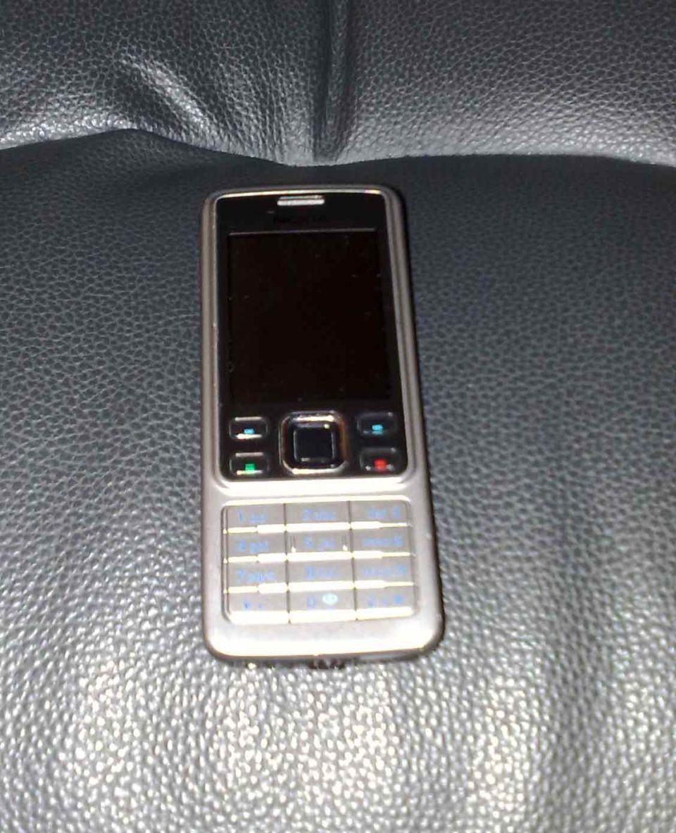 Silver cell phone with a black screen and silver keypad on a dark textured surface