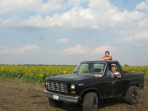1985 Ford Bronco - Two people are in and on a black pickup truck with a sunflower field in the background.