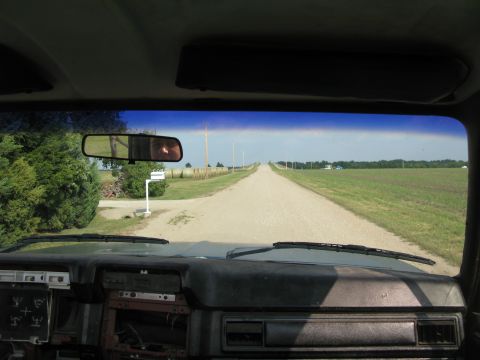 1985 Ford Bronco - Driving down a long, straight dirt road through agricultural fields, as seen from the driver's seat.