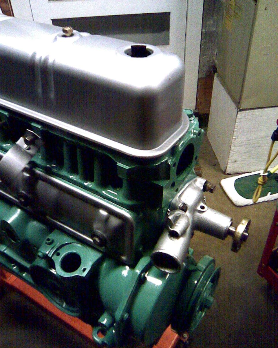 Close-up of a green engine block with a silver valve cover and some attached metal components