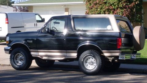 1996 Ford Bronco - Side view of a black 1996 Ford Bronco with a tan removable top and spare tire on the back.