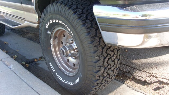 Close-up of a BFGoodrich All-Terrain T/A tire and wheel on a vehicle, parked near a curb