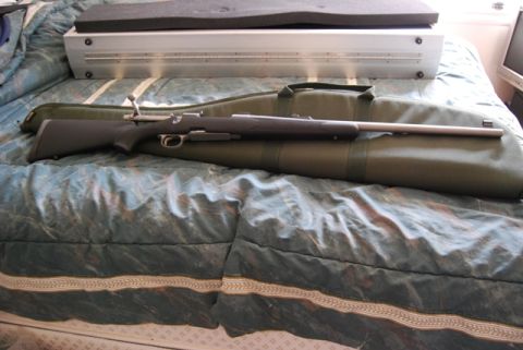1991 Ford Bronco - A rifle lies on a green gun bag, placed on a bed with a metal case behind it.