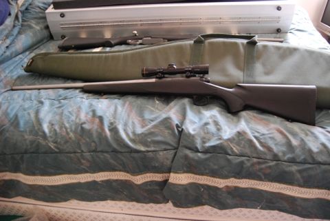 1991 Ford Bronco - A rifle with a scope is laid out on a bed with two gun cases behind it.