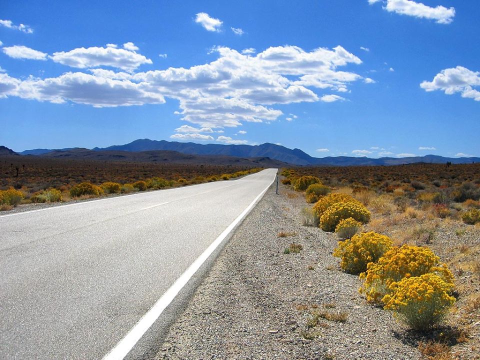 long, empty highway stretching into the distance through a desert landscape with mountains in the background