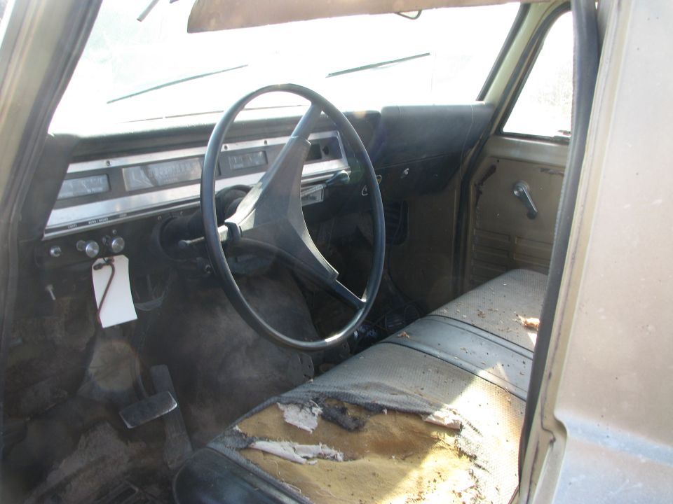 Dusty vintage International truck interior with two-spoke wheel and torn bench seat