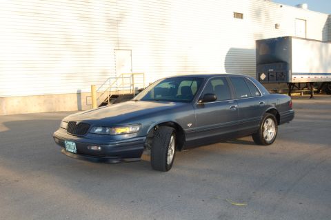 1985 Mercury Grand Marquis - This sedan, likely a late 1990s model, is parked in front of a commercial building.