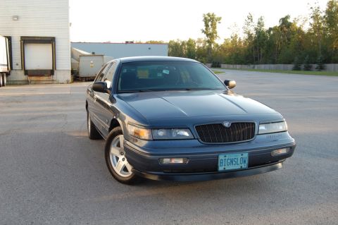 1985 Mercury Grand Marquis - A dark blue Mercury Grand Marquis is parked outside a warehouse.