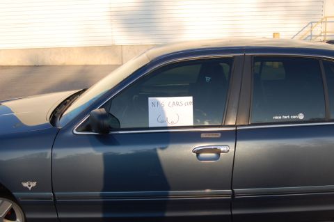 1985 Mercury Grand Marquis - Side view of a dark blue sedan with a sign on the window and a sticker on the rear window.