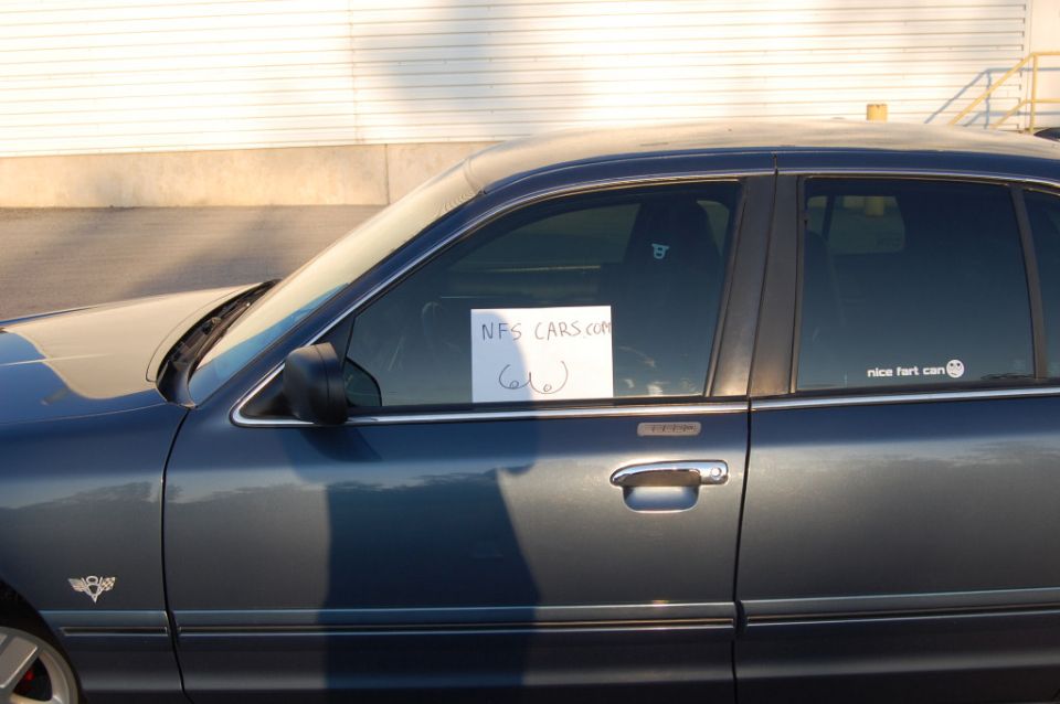 Side view of dark blue sedan with handwritten 'NFS CARS.COM' sign in window