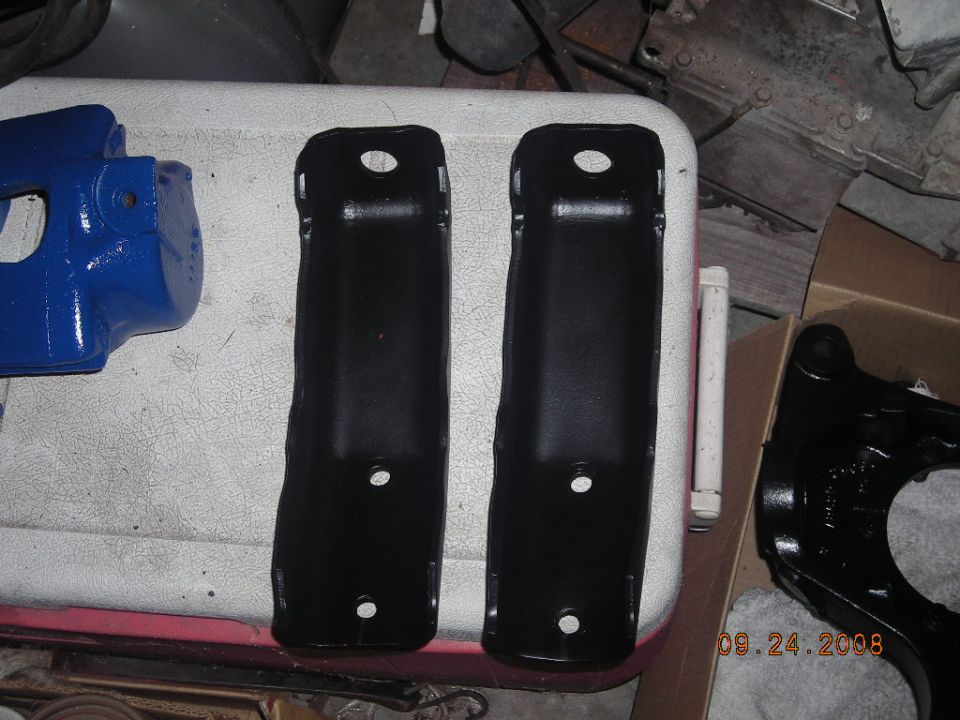 Two black metal brackets and a blue painted part sit on a white surface