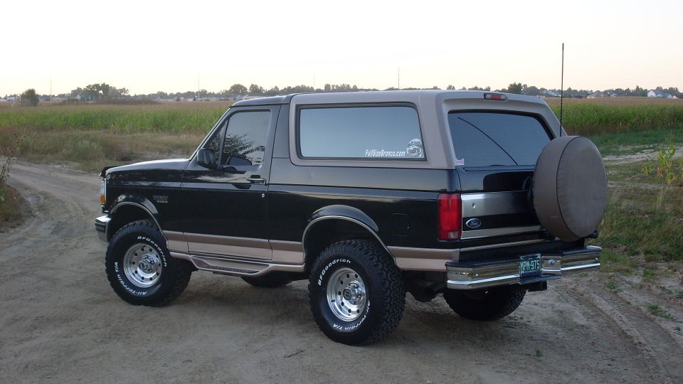 Black and tan 1996 Ford Bronco with a spare tire on the rear, parked on a dirt road