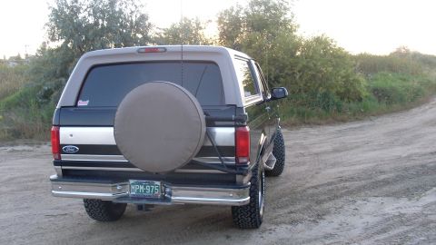1996 Ford Bronco - This Ford Bronco is parked on a dirt road with brush in the background.