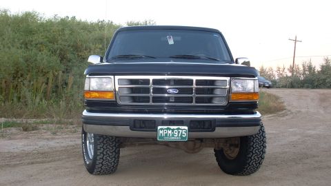 1996 Ford Bronco - This Ford Bronco is shown from the front, parked on a dirt road with vegetation in the background.