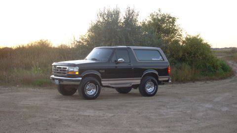 1996 Ford Bronco - Black 1996 Ford Bronco sits parked on a dirt road during the day.