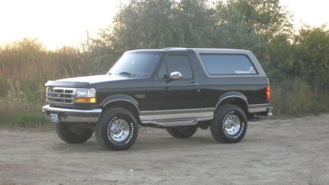 1996 Ford Bronco - A black Ford Bronco is parked on a dirt road with vegetation in the background.