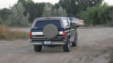 1996 Ford Bronco - Rear view of a 1996 Ford Bronco on a dirt road with a spare tire mounted externally.