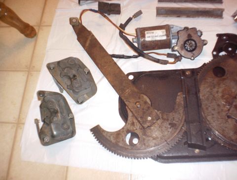 1986 Ford Bronco - Various metal parts for a vehicle window regulator are laid out on a white surface.