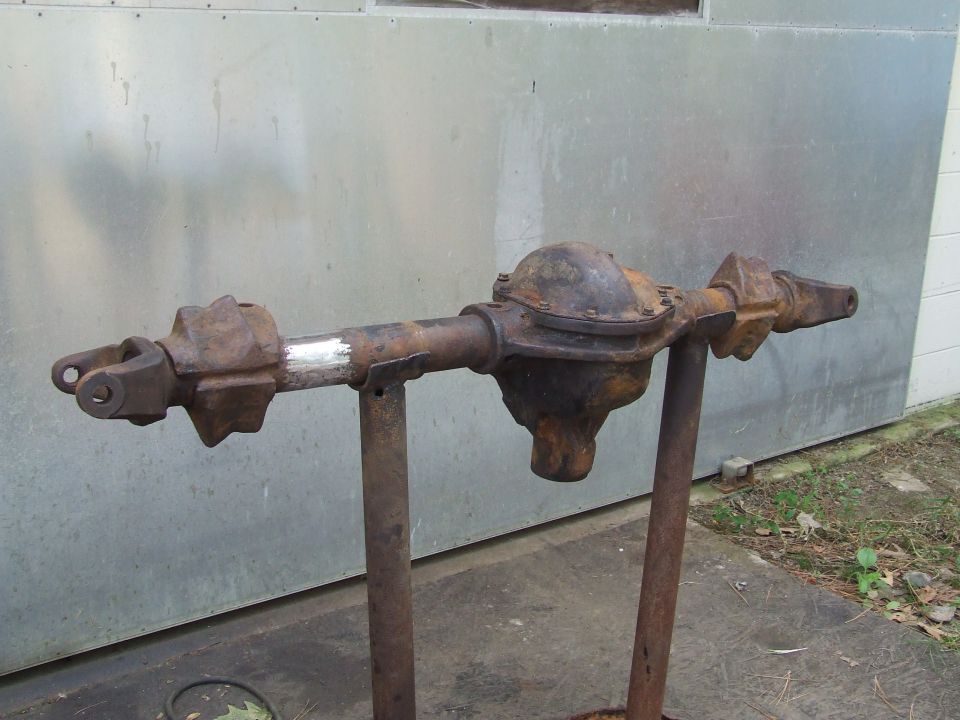 Rusty rear axle assembly on stands, with a section of pipe that has been cleaned and painted silver