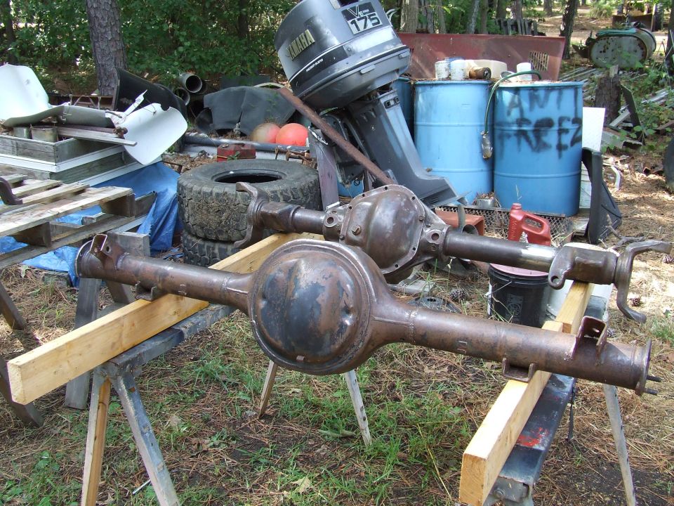 Two rusty rear axles are on sawhorses outdoors. A Yamaha outboard motor is behind them