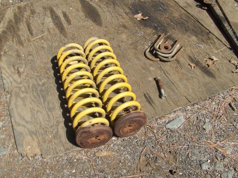 1967 Ford Bronco - Two yellow coil springs and assorted hardware are laid out on a weathered wooden surface, likely for a vehicle repair or restoration projec…