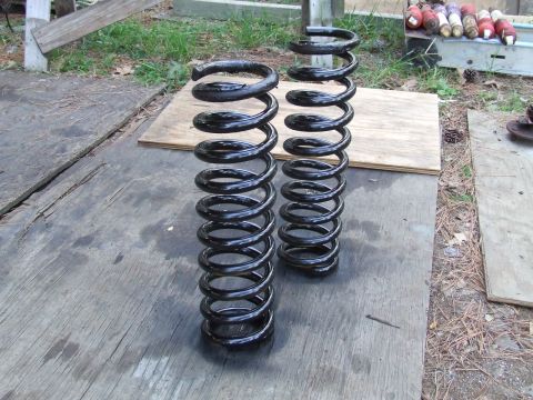 1967 Ford Bronco - Two black coil springs are shown on a wooden surface, with grass and debris in the background.