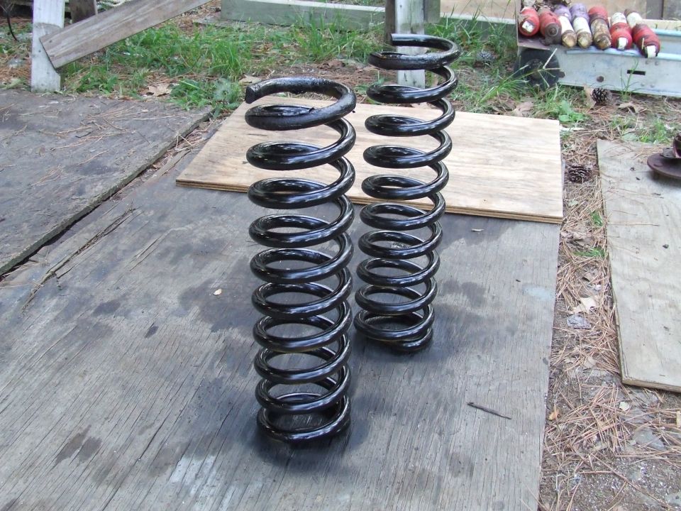 Two black coil springs, one taller than the other, resting on a wooden surface outdoors