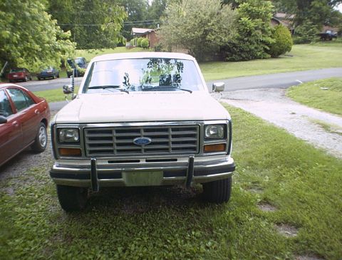 1986 Ford Bronco - A white Ford truck is parked on a grassy area next to a gravel driveway.