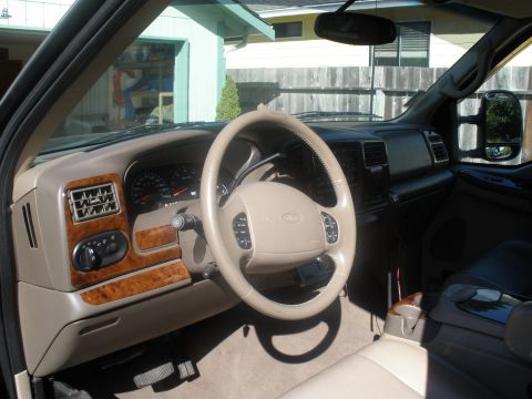 2002 Ford Excursion - The interior of a 2002 Ford Excursion shows a tan dashboard with wood accents and a Ford steering wheel.