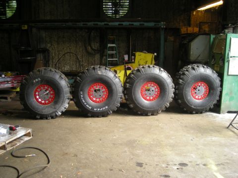 1979 Ford Bronco - Four Super Swamper tires with red rims are displayed in a workshop setting.