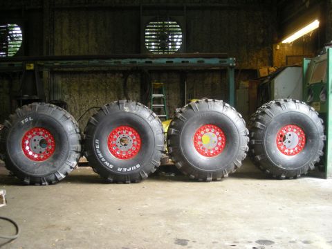 1979 Ford Bronco - Four large off-road tires with red rims are displayed in a workshop setting. One tire is labeled 'Super Swamper'.