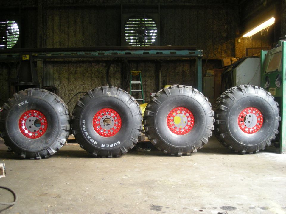Four large off-road tires with red rims, one labeled Super Swamper