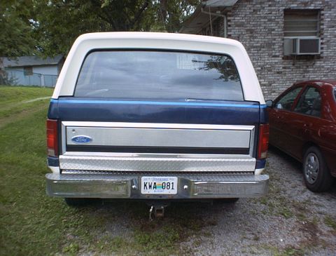 1986 Ford Bronco - Rear view of a blue and white Ford Bronco, parked next to a red car. License plate KWA 081 is visible.