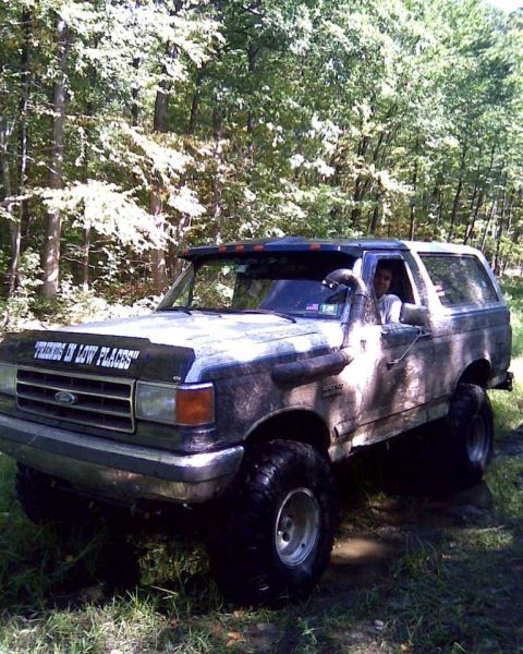 1989 Ford Bronco - Muddy 1989 Ford Bronco navigates off-road terrain with a decal on its hood.
