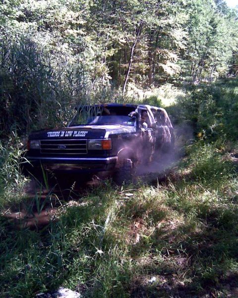 1989 Ford Bronco - A black Ford Bronco navigates a dusty, off-road trail surrounded by dense foliage.