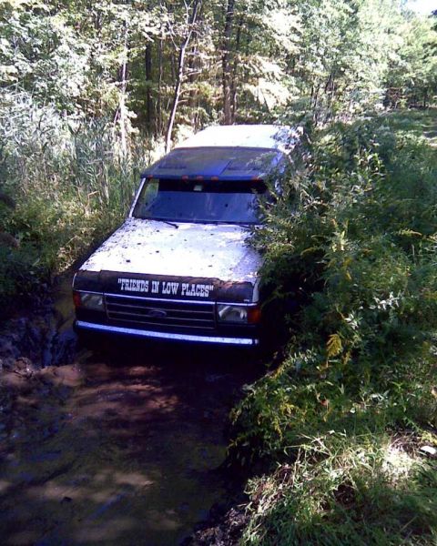 1989 Ford Bronco - This vehicle appears to be stuck in a muddy off-road trail, surrounded by dense foliage.
