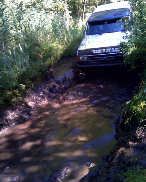 1989 Ford Bronco - A white Ford Bronco navigates a muddy trail, its front grille and hood visible.