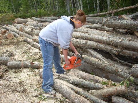 2000 Chevrolet Tahoe - Person operating a chainsaw on a large pile of cut logs in a wooded outdoor setting.
