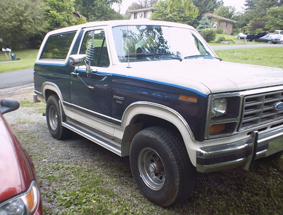 Two-tone blue and white Ford Bronco with chrome trim, parked on gravel