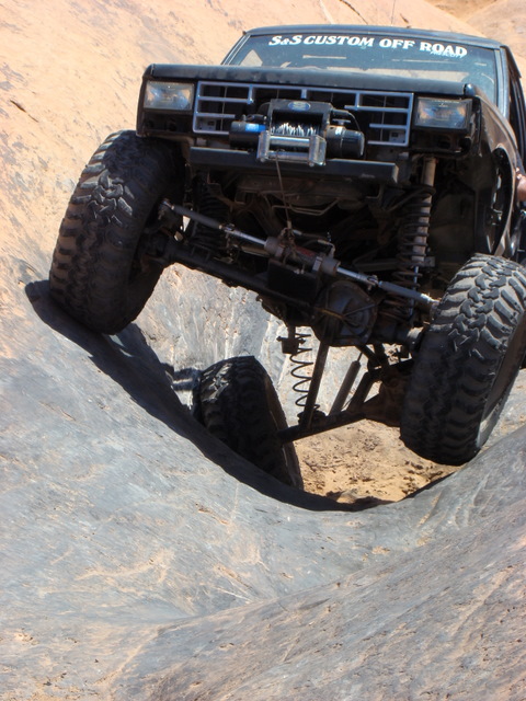 1956 Ford Bronco II - Custom off-road truck with large tires tackles a challenging rocky terrain during an event.