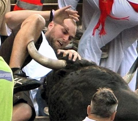 2000 Mercury Grand Marquis - A man is in distress as a bull's horn pierces his leg, surrounded by onlookers in a chaotic scene.