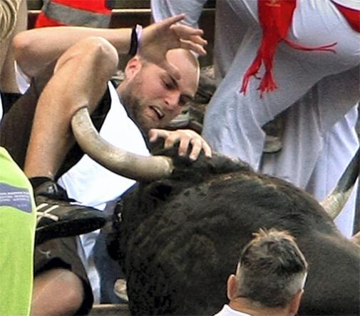 Man in black shirt is gored by a bull's horn, with people in white and red clothing around