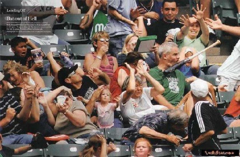 People in stadium seating, some reacting to an event, one holding a baseball bat