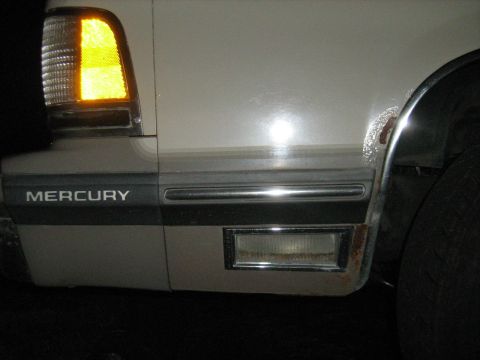 1988 Mercury Grand Marquis - Close-up of the side of a car showing the Mercury emblem and amber turn signal light.